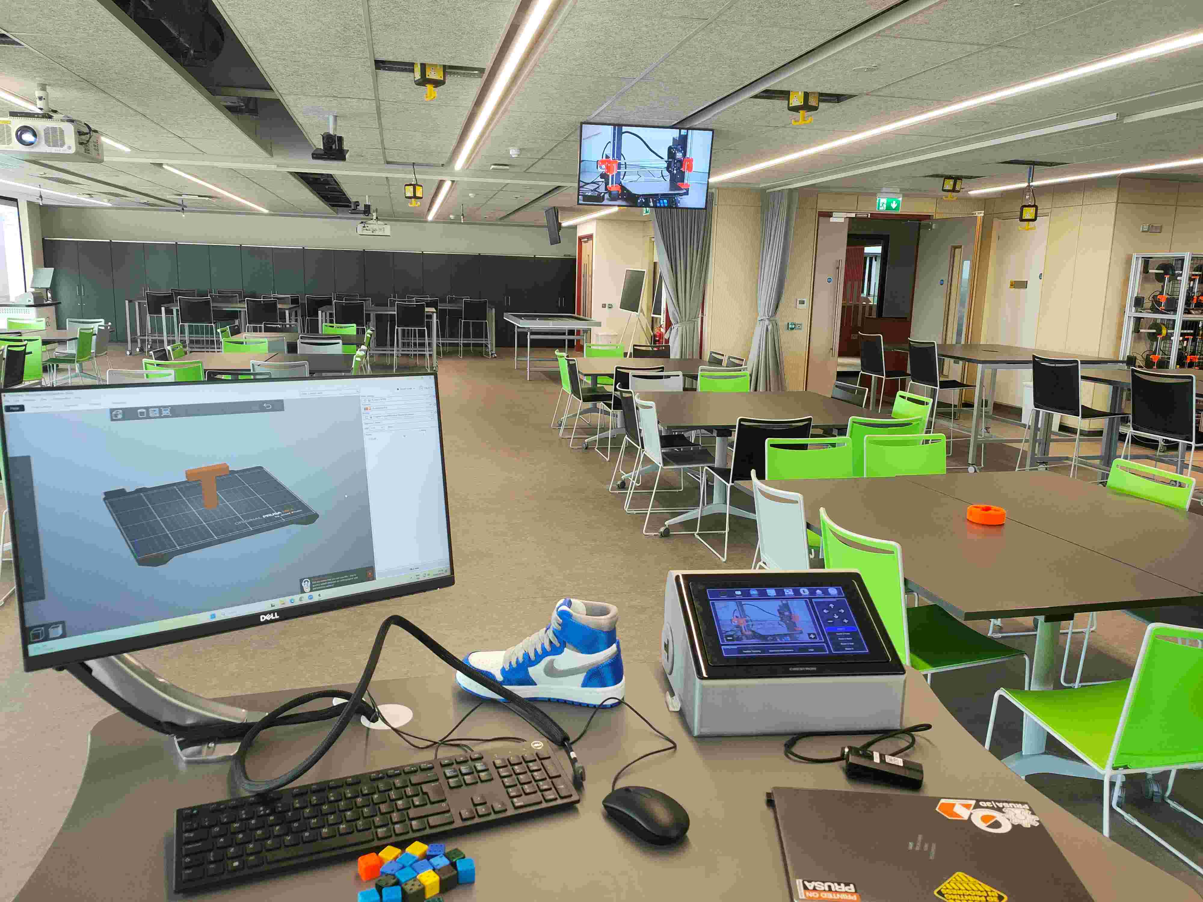 View from the lectern in the classroom — Crestron touchscreen, PrusaSlicer on the monitor showing an STL, and a live 3D printer feed on the wall display.