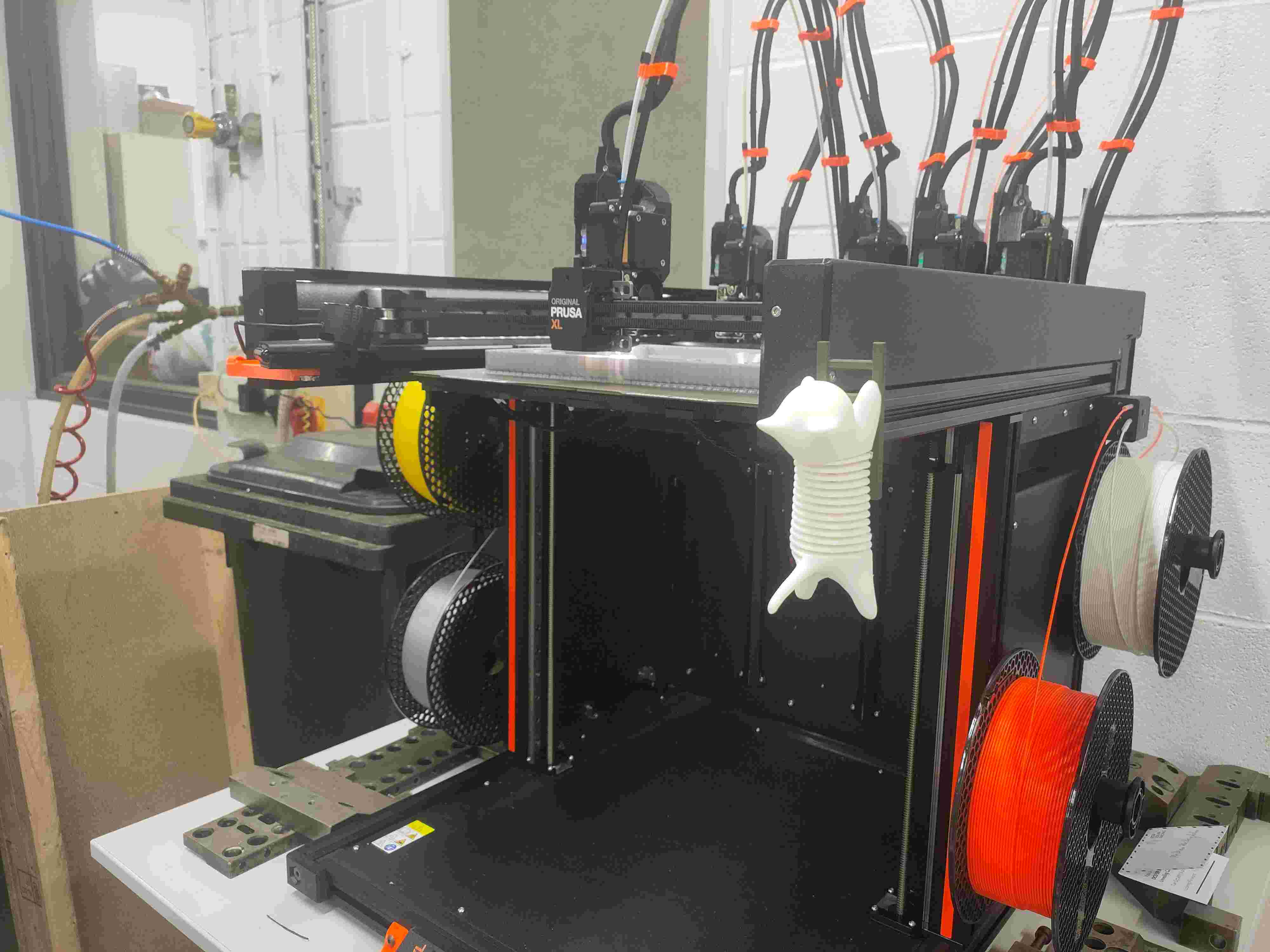 Original Prusa XL multi-tool 3D printer with a five-tool head and a multi-colour print in progress on the side rack.