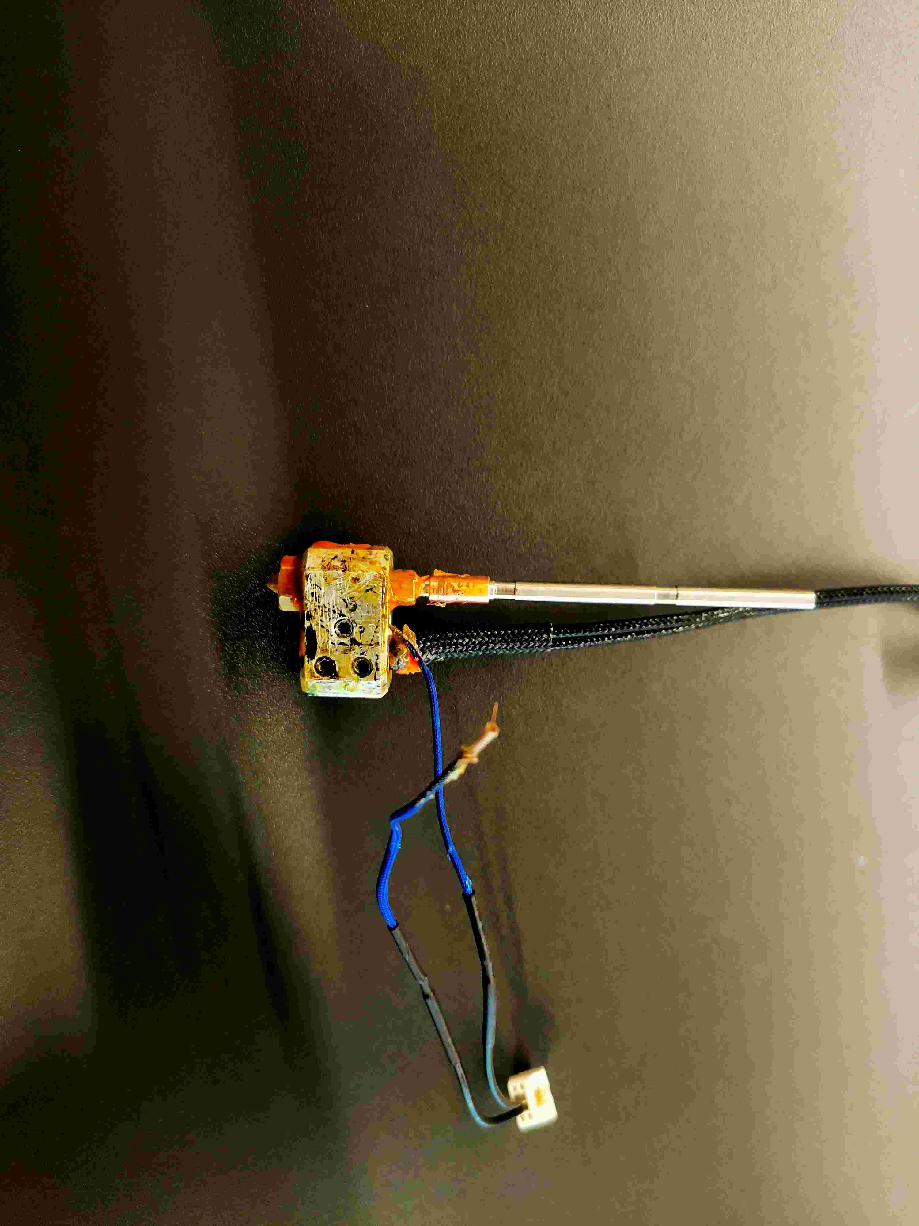 Disassembled Prusa MK4 heater block with carbonised surface residue, heater cartridge, thermistor wires and JST connector.