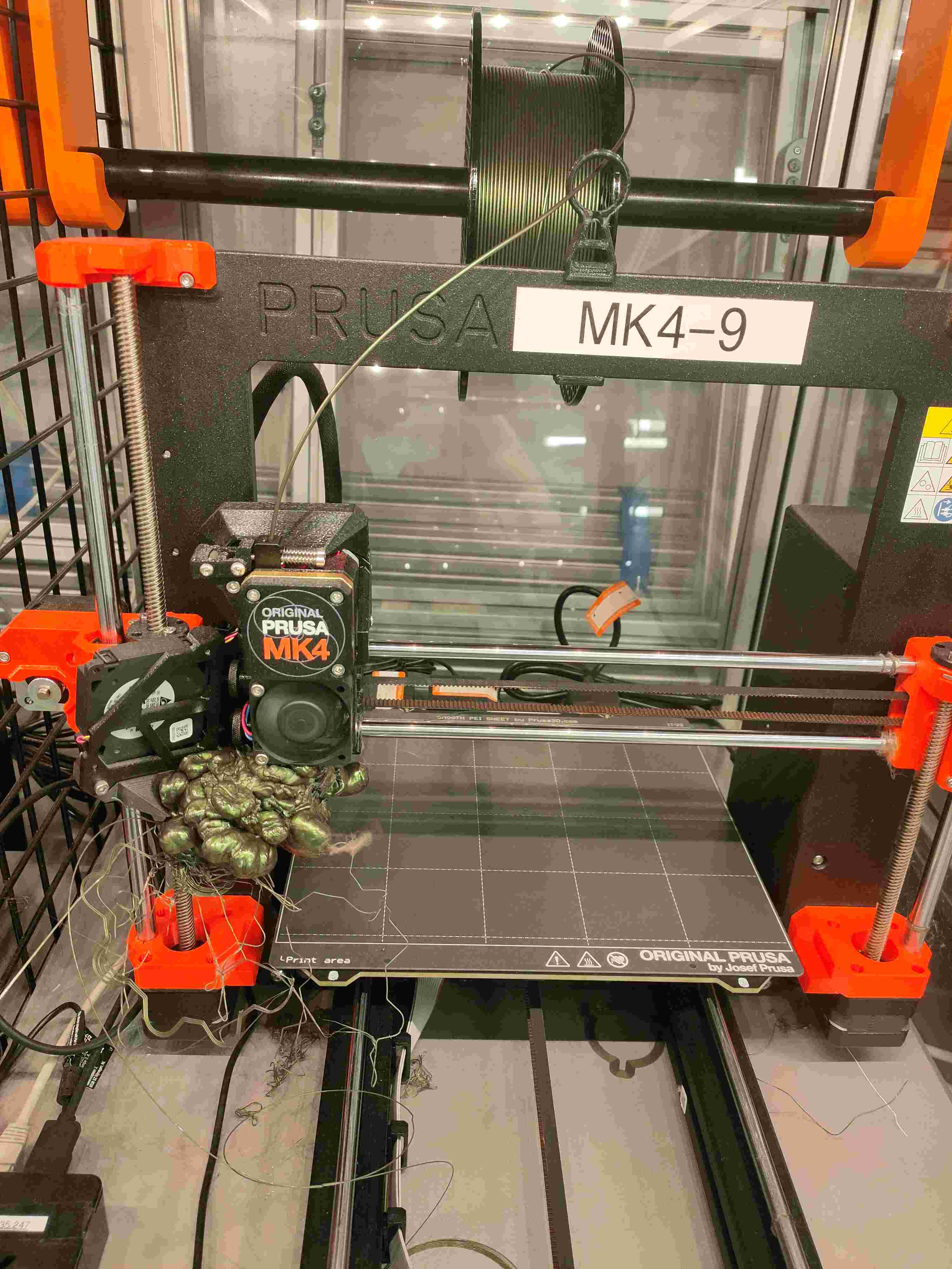 Prusa MK4-9 with a catastrophic blob of bronze-green filament engulfing the hotend after the print detached from the build plate.